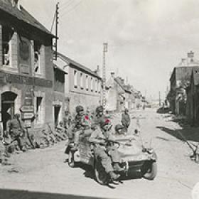 Members of the 101st Airborne Travel through a French Village in a Captured German Car