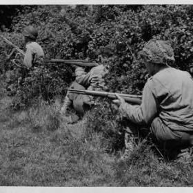 Taking cover in the bushes this allied sniper patrol searches nearby trees and shrubs for any enemy soldiers waiting to ambush them. 